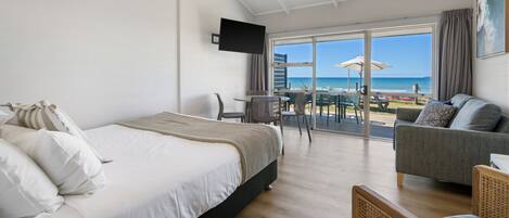 Een slaapkamer met een bed, een bank en een televisie. Er is uitzicht op het strand vanuit het raam.