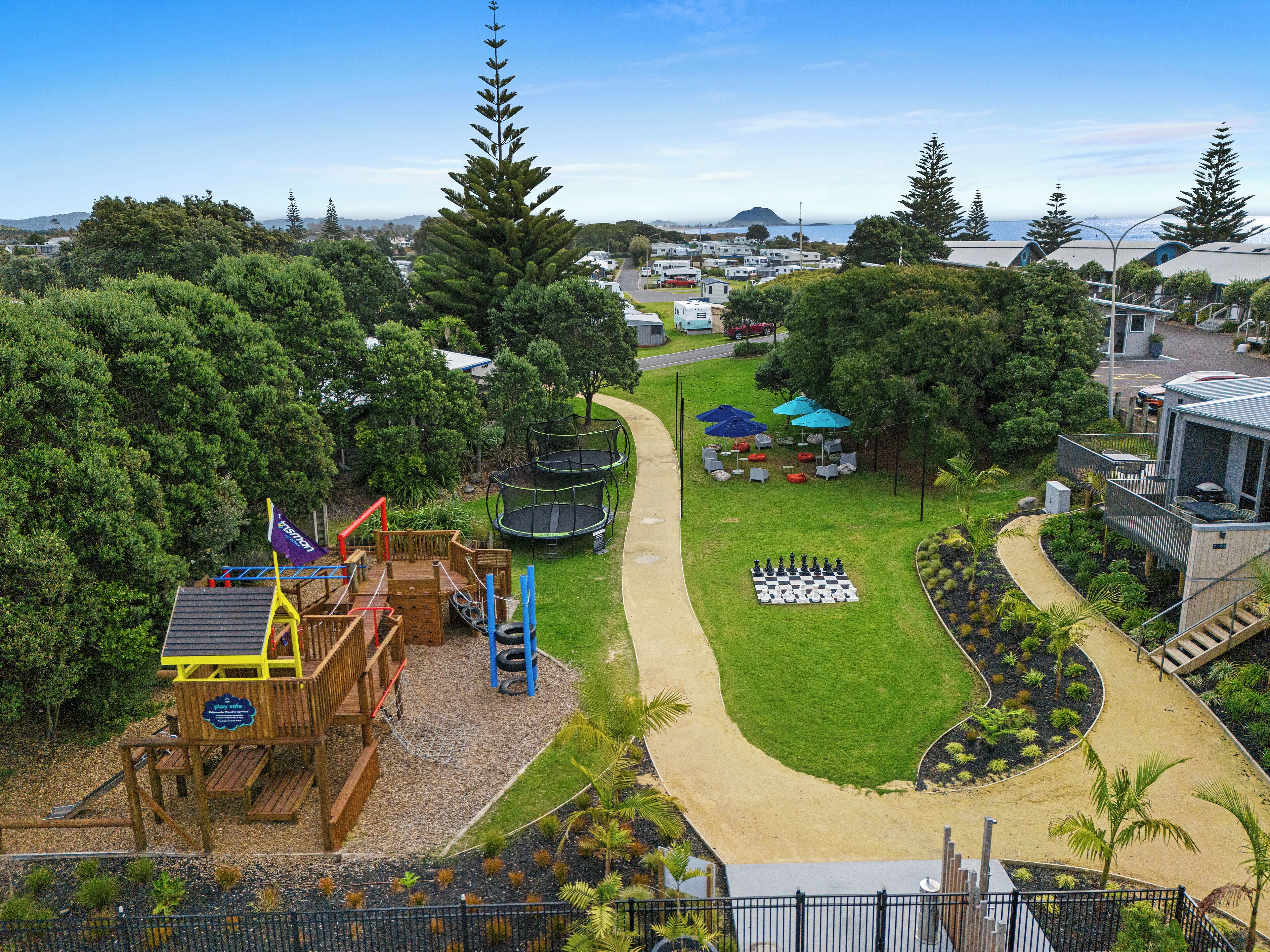 A playground with a play structure, a chessboard, and a picnic area with umbrellas.