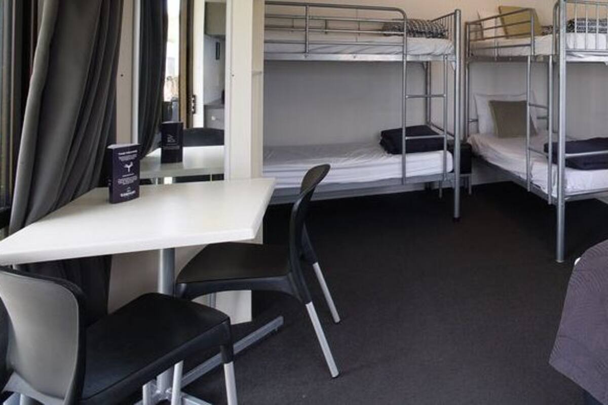 Ein Schlafraum mit Etagenbett, Schreibtisch und Stuhl, einem Fenster mit Vorhängen und einem Bett mit grauer Decke.