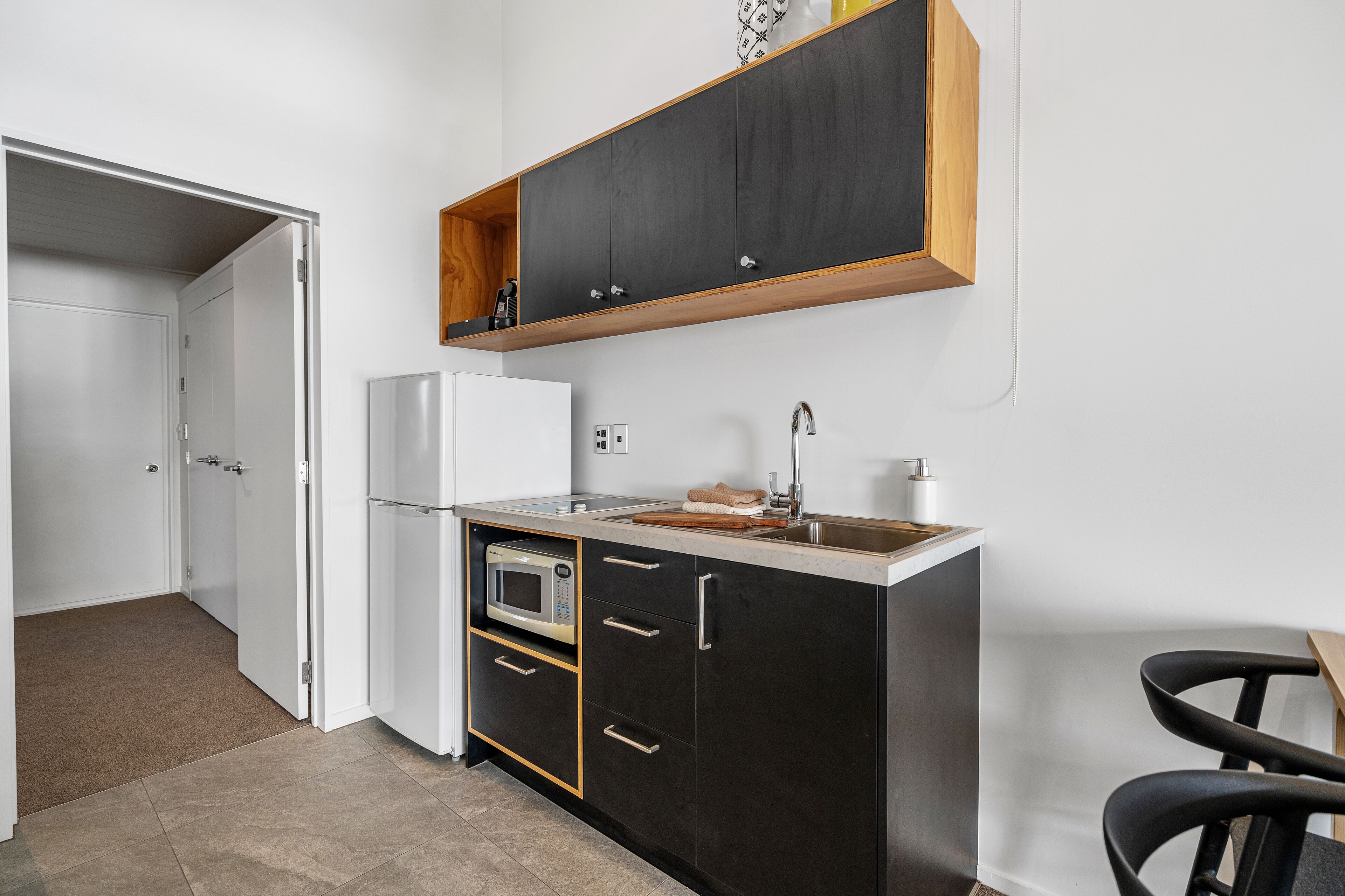A compact kitchen with a microwave, refrigerator, and wooden countertop.