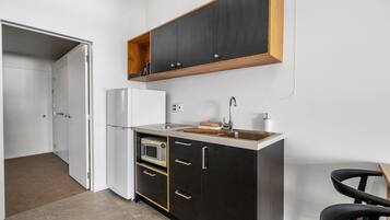 A compact kitchen with a microwave, refrigerator, and wooden countertop.