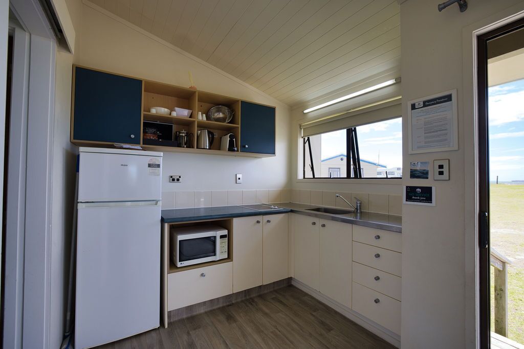 Una cocina compacta con refrigerador, microondas, pileta y estantes de madera.