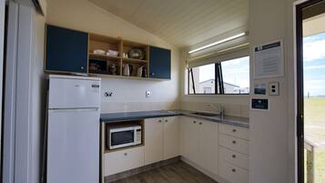 Una cocina compacta con refrigerador, microondas, pileta y estantes de madera.