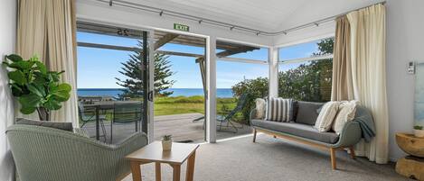 A room with a view of the sea, a sofa, a chair, and a small table.
