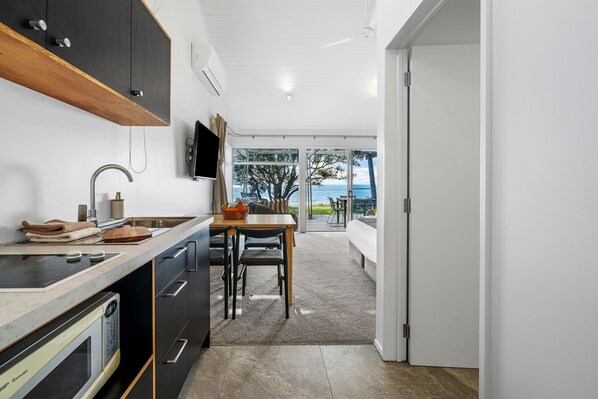 A modern kitchen with a built-in oven, a dining area with a table and chairs, and a view of the ocean through large glass doors. - Tasman Holiday Parks - Papamoa Beach (Tauranga)