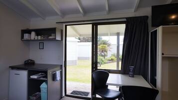 Una kitchenette compacta con refrigerador, un lavamanos pequeño y una encimera. Hay una zona de comedor con una mesa y dos sillas. Un televisor está montado en la pared sobre la mesa.