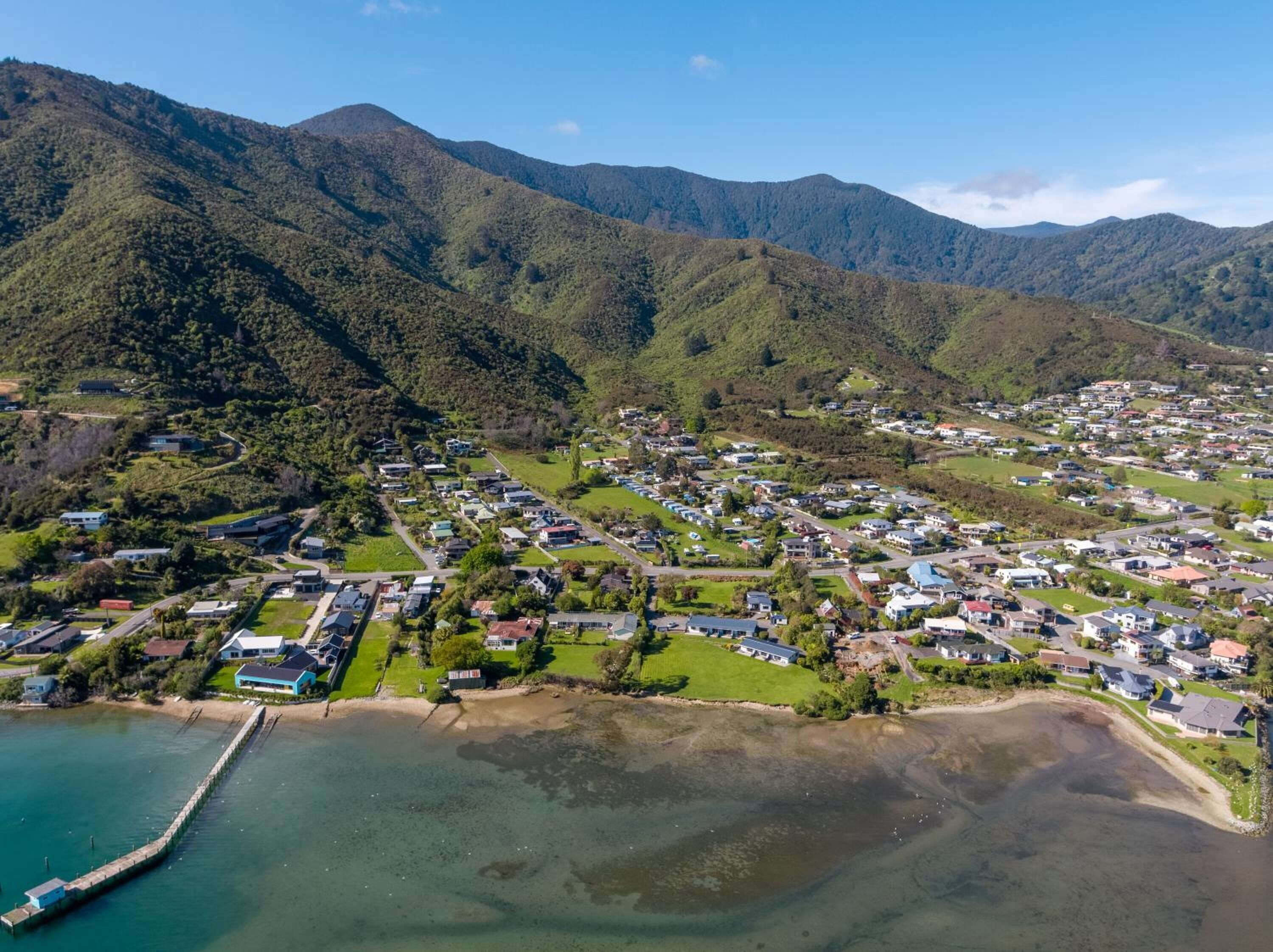Zona residencial costera con casas, un muelle y montañas al fondo.