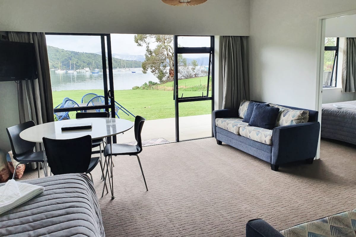Un salon moderne avec un canapé, une table à manger et des chaises. Une grande fenêtre offre une vue sur un lac et des bateaux.