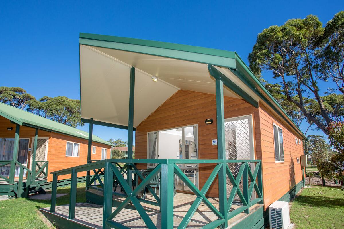A wooden cabin with a covered porch, a sliding glass door, and a small outdoor seating area.