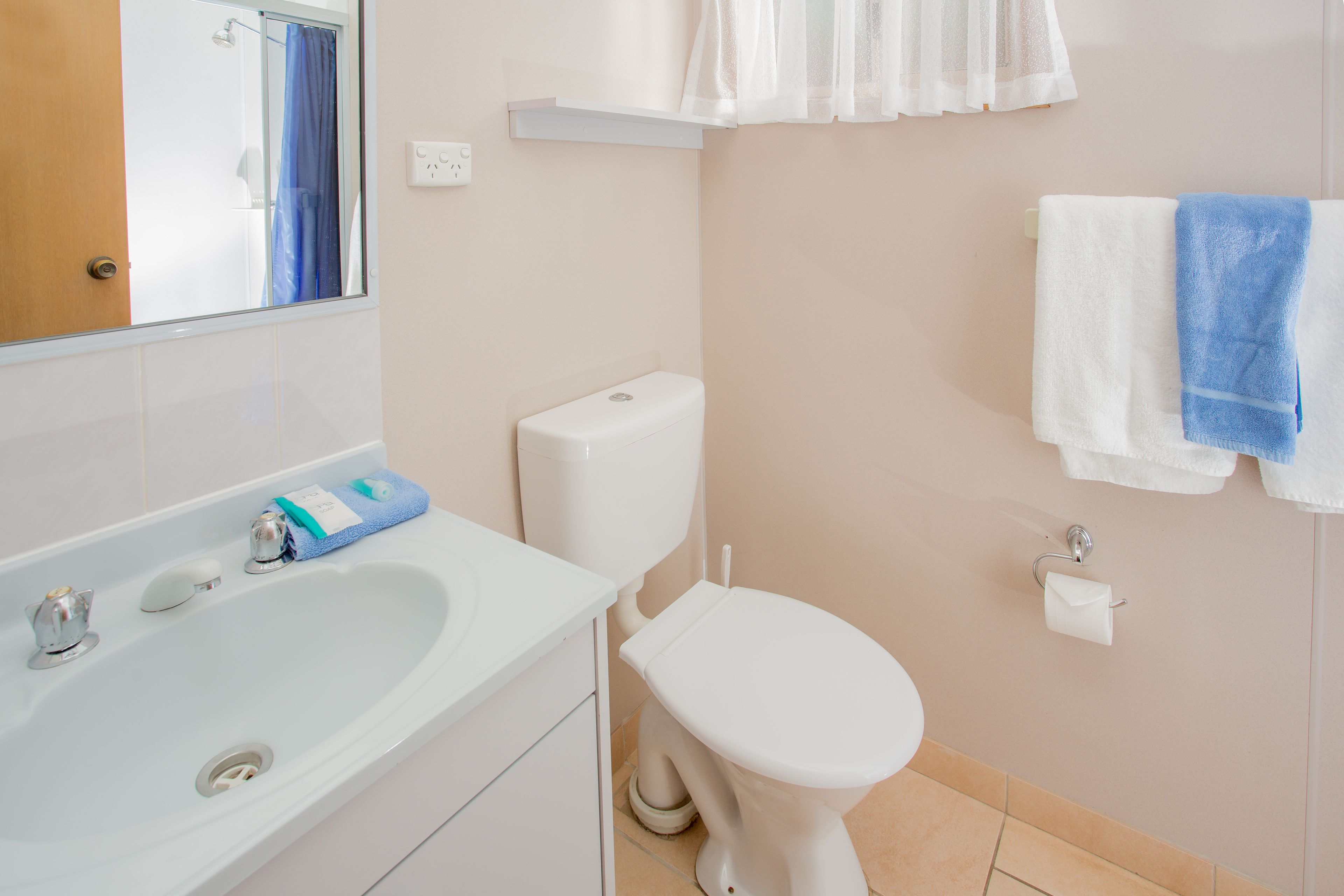 Un baño con lavamanos blanco, inodoro y toallero con toallas.