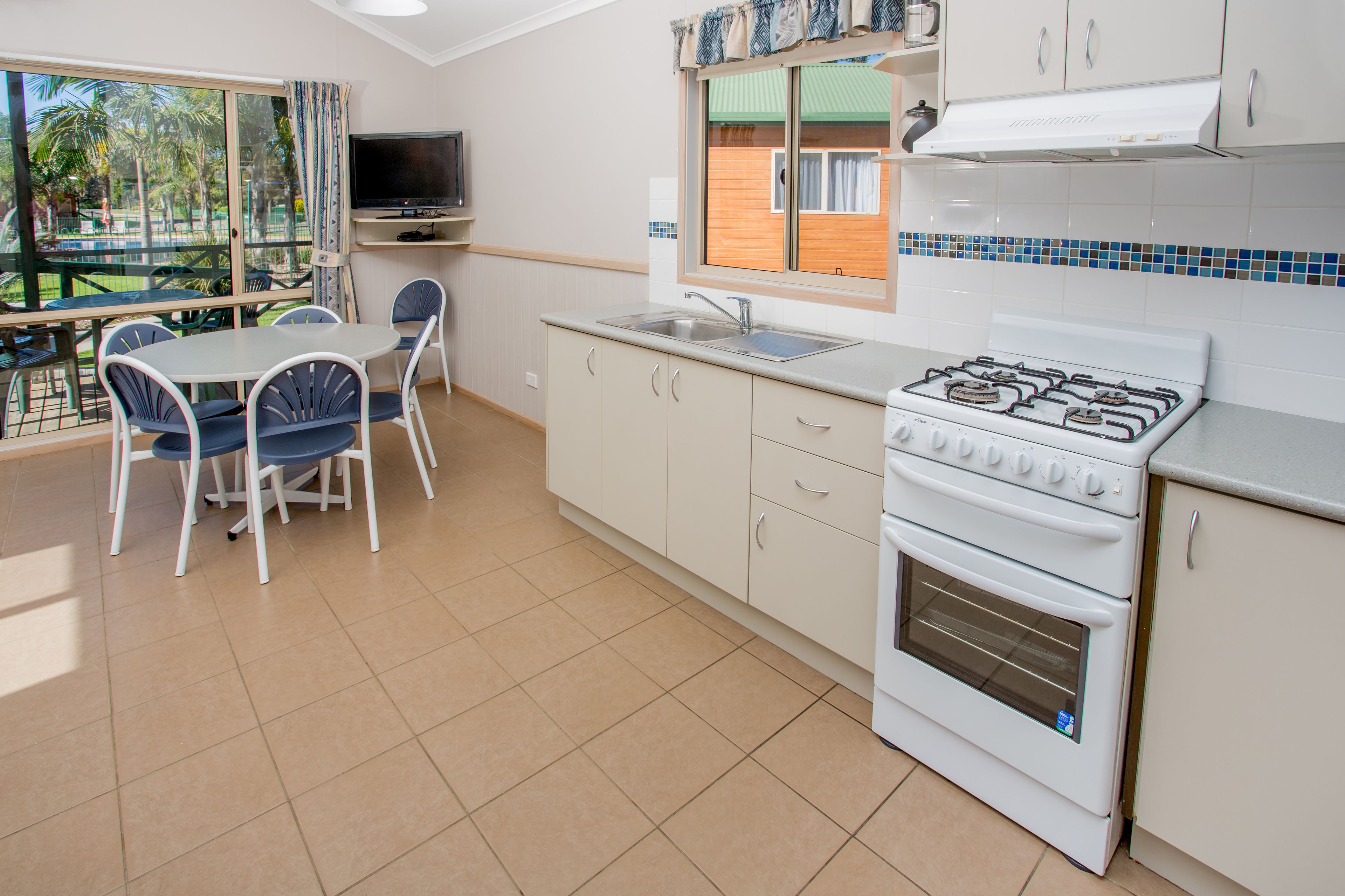 A kitchen with a gas stove, oven, sink, and dining area with chairs and a table.