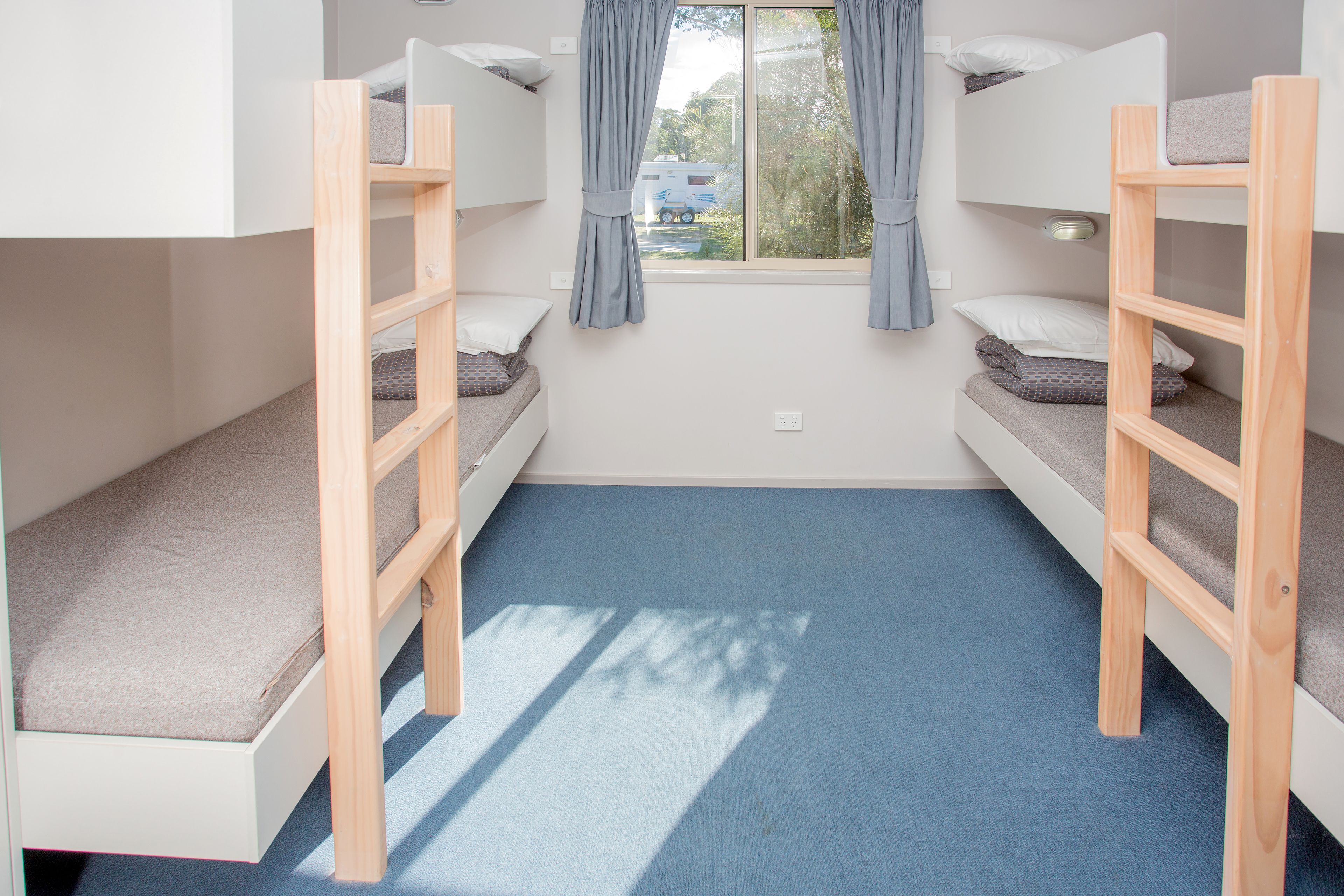 Una habitación con dos literas, una ventana con cortinas y una alfombra azul.