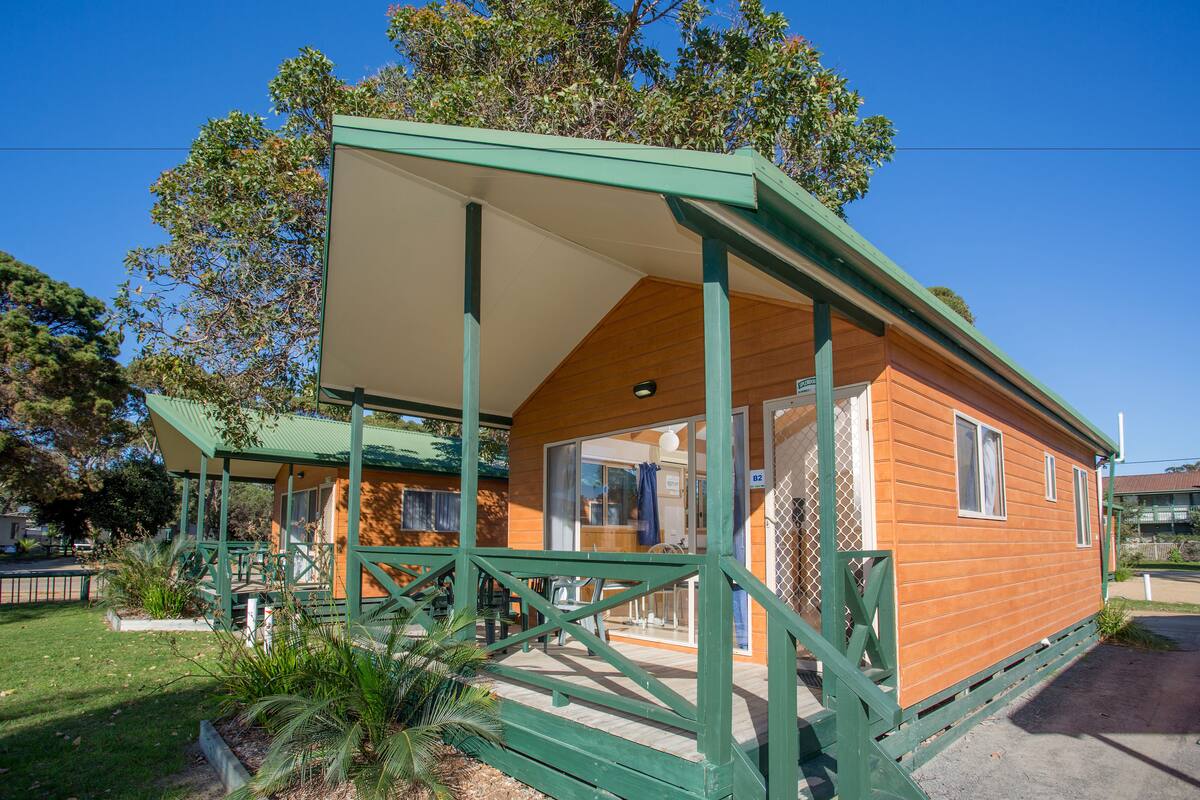 A small wooden cabin with a green porch and a covered patio area.