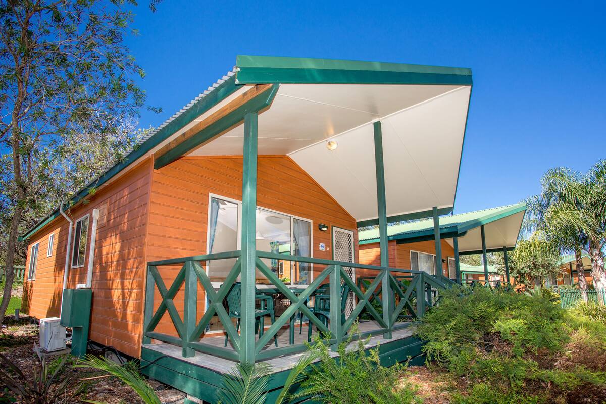 A wooden cabin with a covered porch and a fenced deck area.