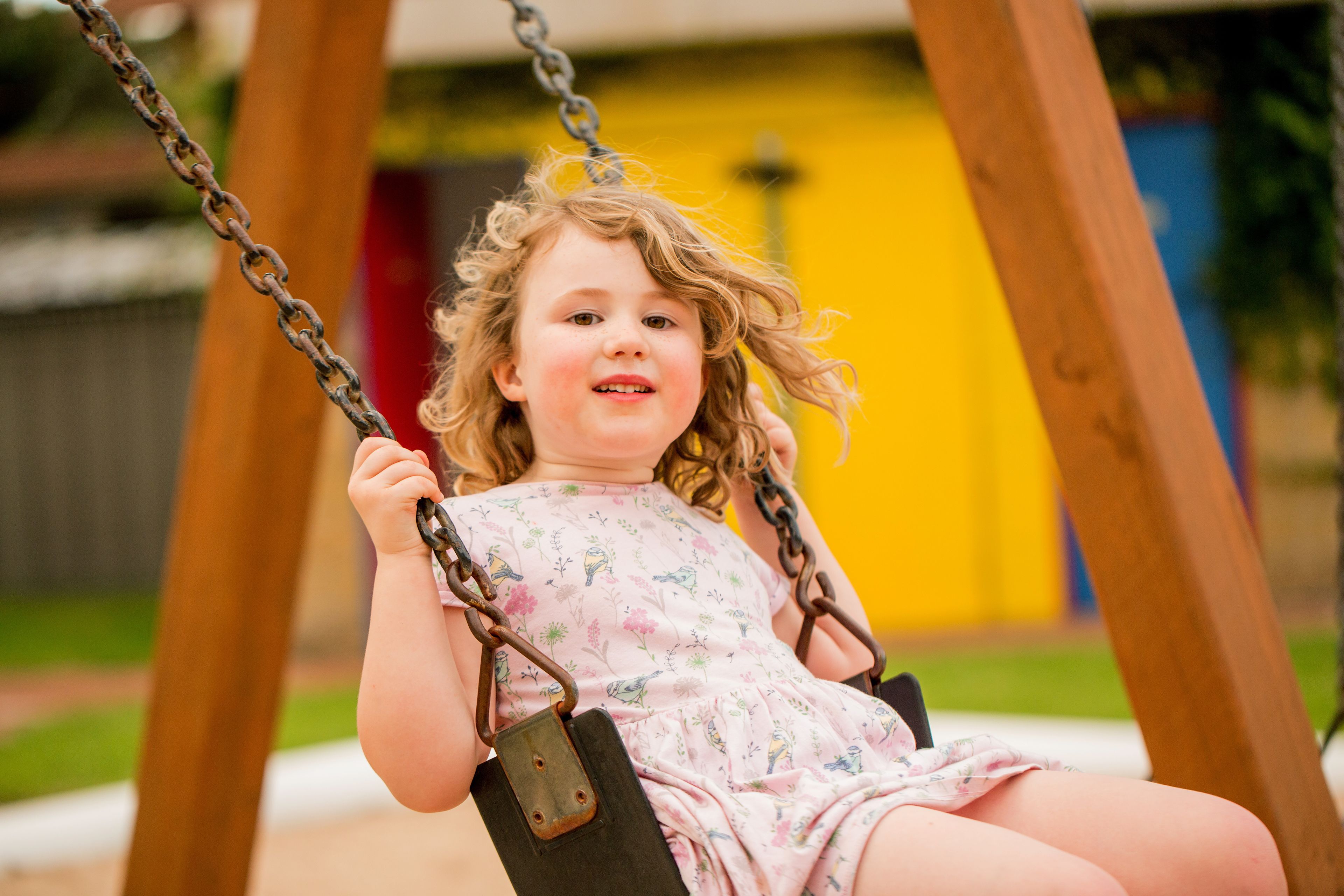 A child on a swing with a wooden frame and metal chains.