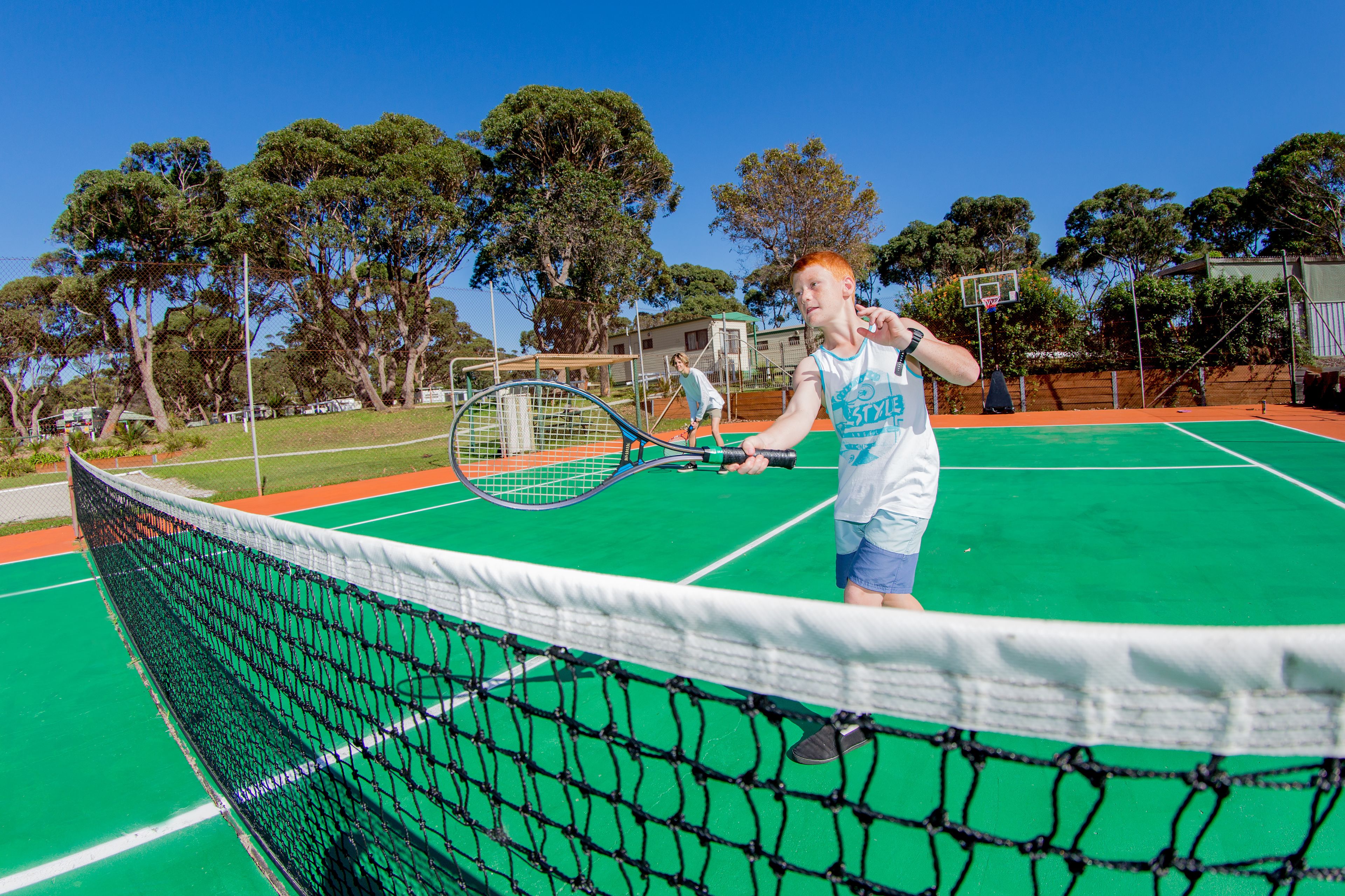 Un campo da tennis con una rete, alberi e un edificio sullo sfondo.