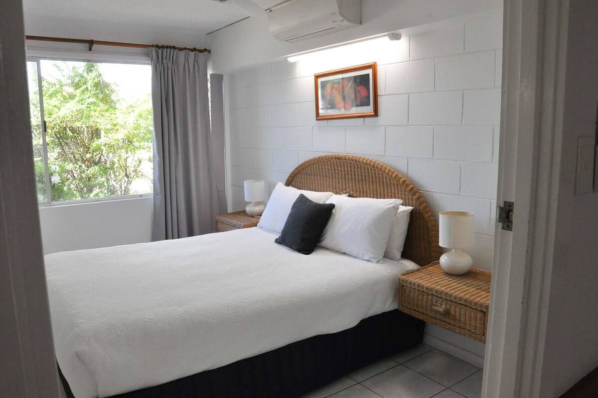 Une chambre à coucher bien rangée, avec un grand lit, une table de chevet avec une lampe et un tableau encadré au mur.