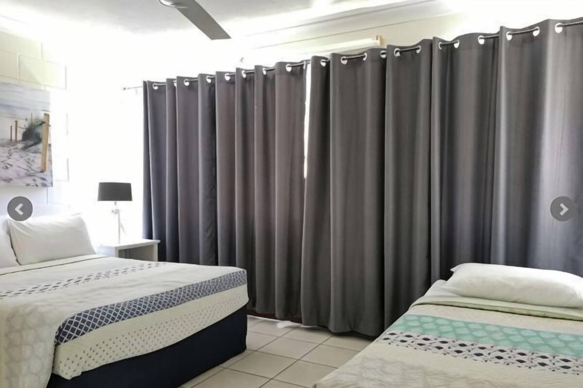 Une chambre à coucher avec un lit, une table de chevet, une lampe et une fenêtre avec des rideaux.