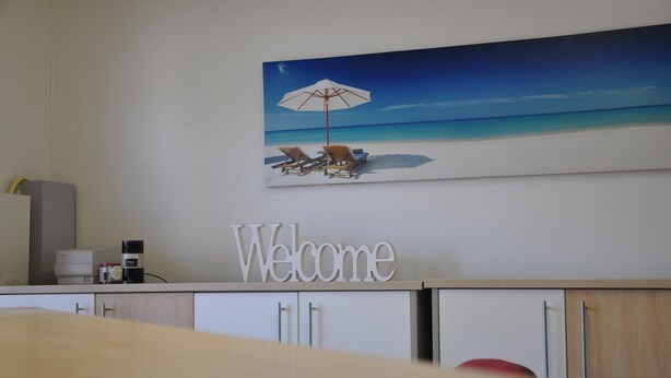 A reception desk with a 'Welcome' sign, a painting of a beach scene, and a coffee machine. - Palm Waters Holiday Villas (North Ward)