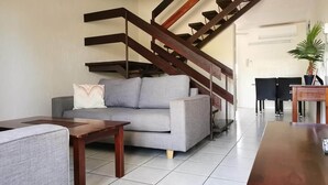 A living room with a grey sofa, wooden coffee table, and a staircase with dark wooden railings. - Palm Waters Holiday Villas (North Ward)