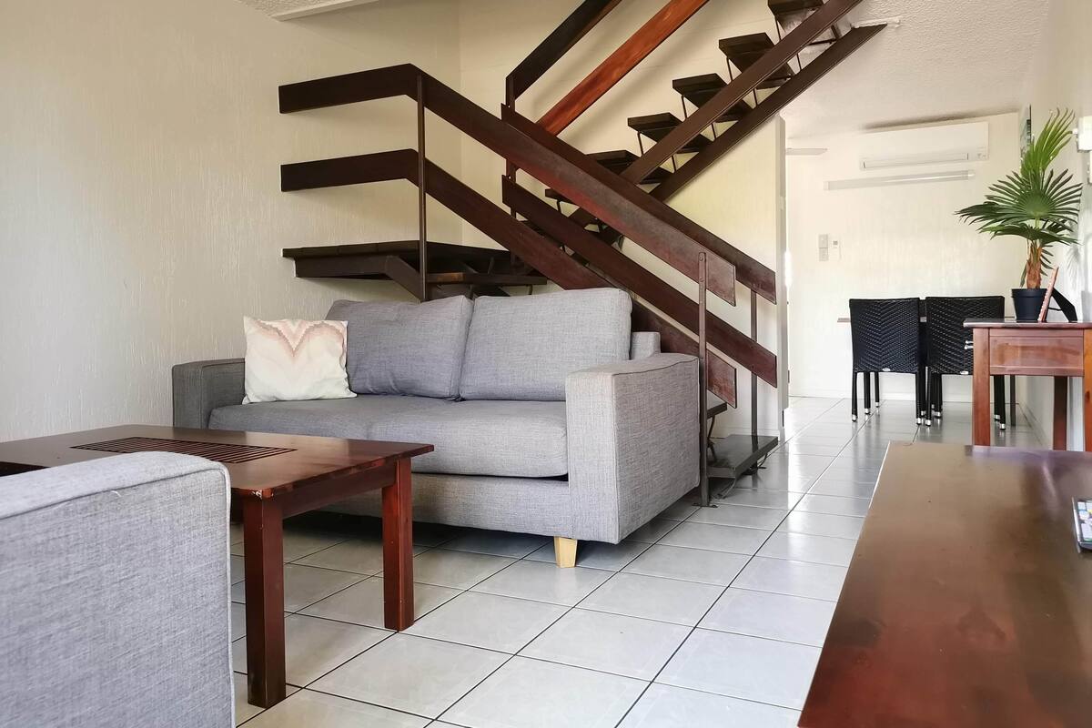 Un salon avec un canapé gris, une table basse en bois et un escalier doté de rampes en bois foncé.