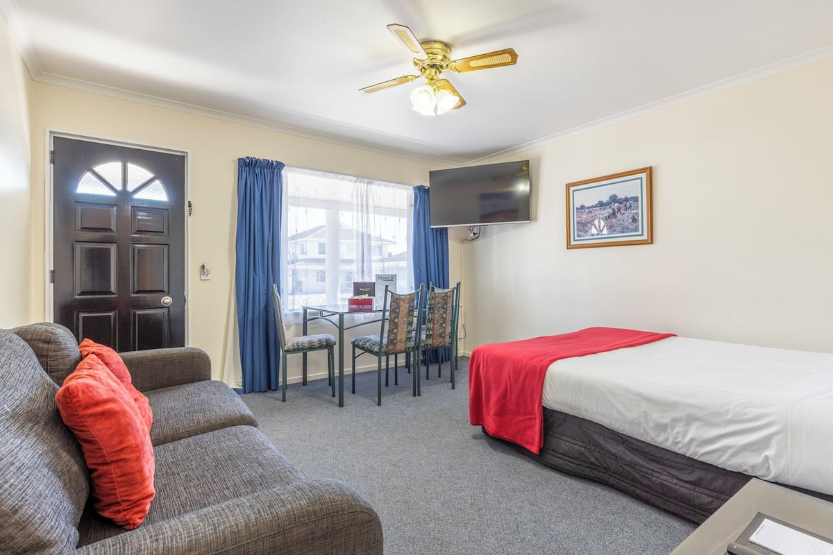 Une chambre d’hôtel équipée d’un lit, d’un canapé, d’un bureau avec des chaises, d’une télévision et d’un ventilateur de plafond.