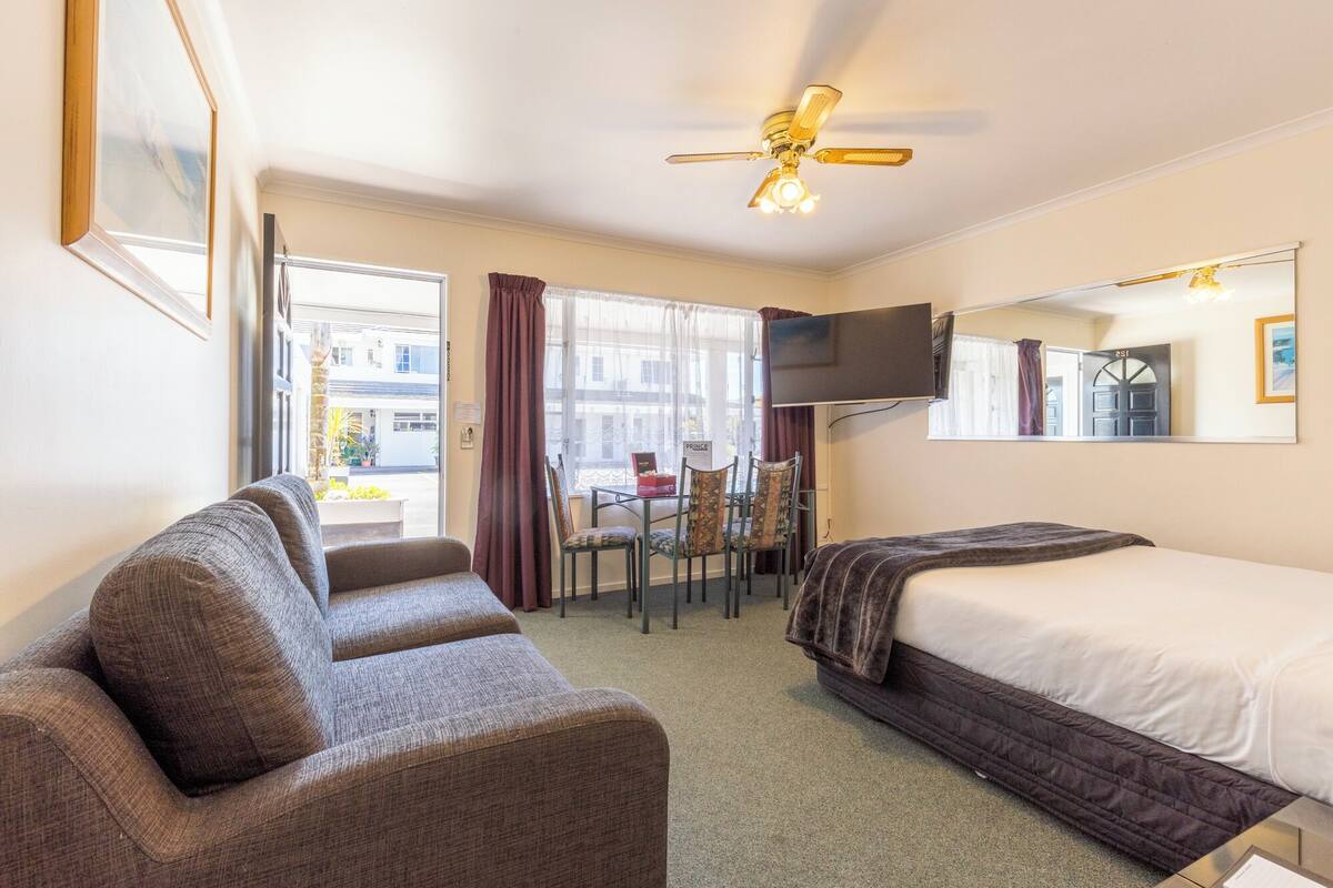 Une chambre d’hôtel équipée d’un lit, d’un canapé, d’une télévision, d’un ventilateur de plafond et d’une fenêtre avec des rideaux.