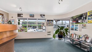 A reception area with a wooden desk, a potted plant, and a magazine rack. - ASURE Prince Motor Lodge (Taupo)