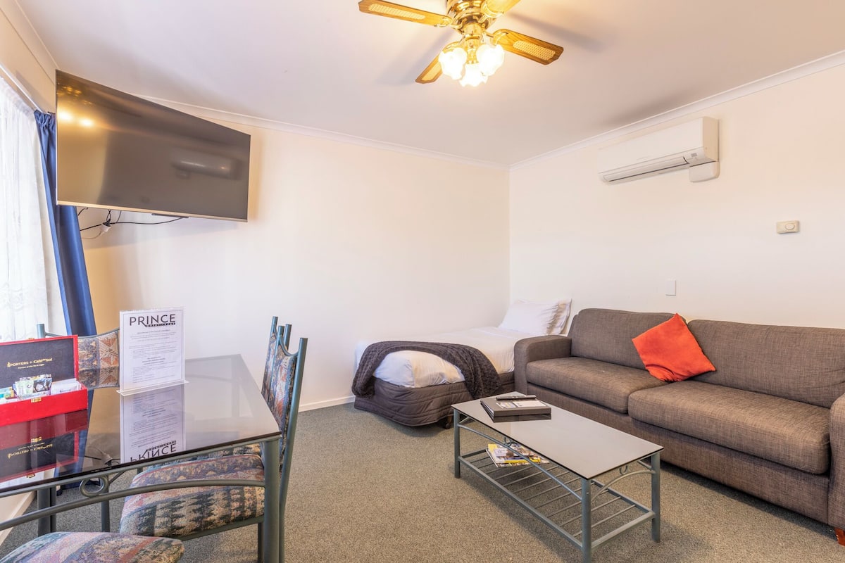 Un salon comprenant un canapé, une table basse, un téléviseur fixé au mur et un ventilateur de plafond.
