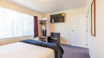 A hotel room with a bed, a desk with a chair, a wardrobe, and a TV mounted on the wall.