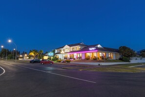 Un hotel su due piani con un cartello 'Prince', un ristorante chiamato 'Thai Restaurant & Bar' con insegne al neon e un parcheggio con diverse auto.