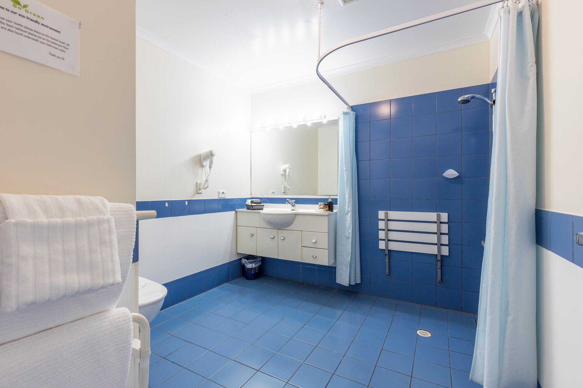 Ein Badezimmer mit blauen Fliesen, einem weißen Waschbecken, einem Spiegel, einem Handtuchhalter und einer Duschvorhang.