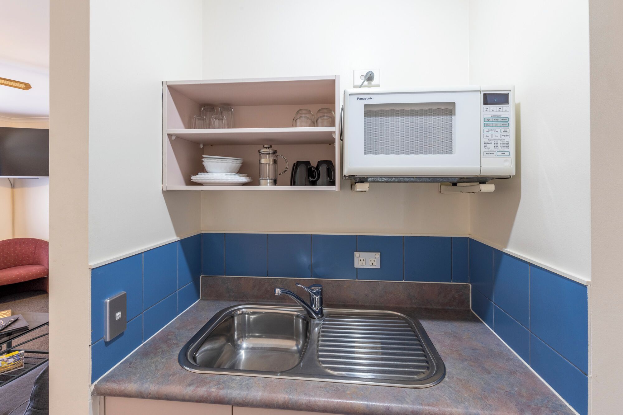 A kitchen with a stainless steel sink, a microwave, and shelves with dishes and glasses.
