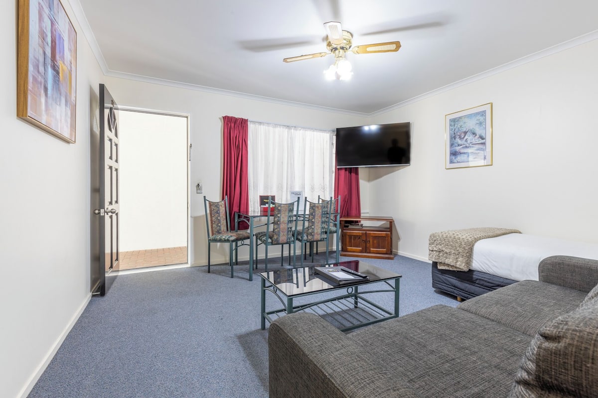Une chambre d’hôtel comprenant un lit, une télévision, une table à manger avec des chaises, un ventilateur de plafond et une porte donnant sur un balcon.