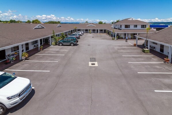 A motel with a central parking lot, multiple rooms with individual driveways, and a view of the mountains in the background. - Prince Motor Lodge (Taupo)