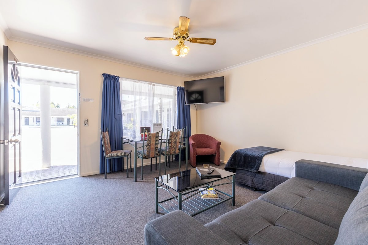 Un salon comprenant un canapé, une table basse, un téléviseur fixé au mur, un ventilateur de plafond et un coin repas avec des chaises et une table.