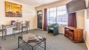 A hotel room with a glass table, a green armchair, a wooden cabinet, and a painting on the wall. - ASURE Prince Motor Lodge (Taupo)
