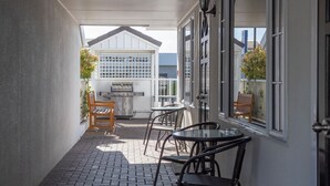 A covered patio with a grill, seating, and a view of a neighboring building. - ASURE Prince Motor Lodge (Taupo)