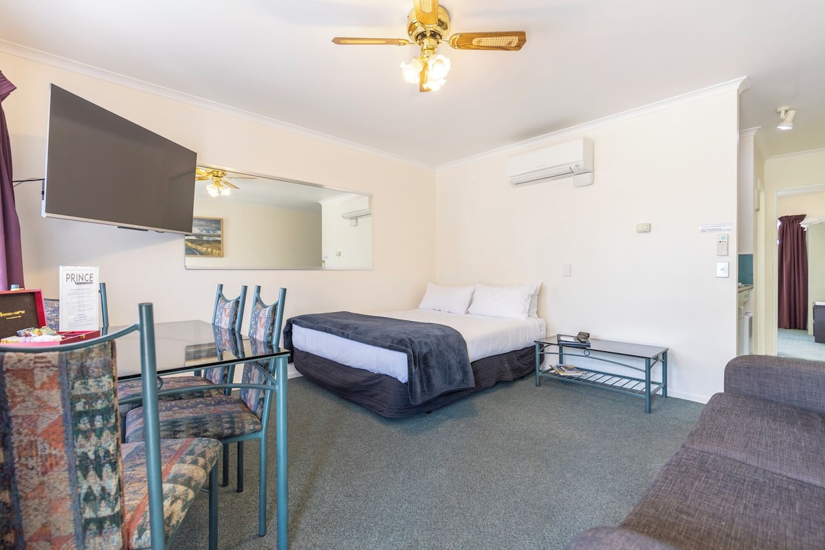 Une chambre d’hôtel équipée d’un lit, d’un bureau, d’une chaise, d’un ventilateur de plafond et d’un grand miroir.