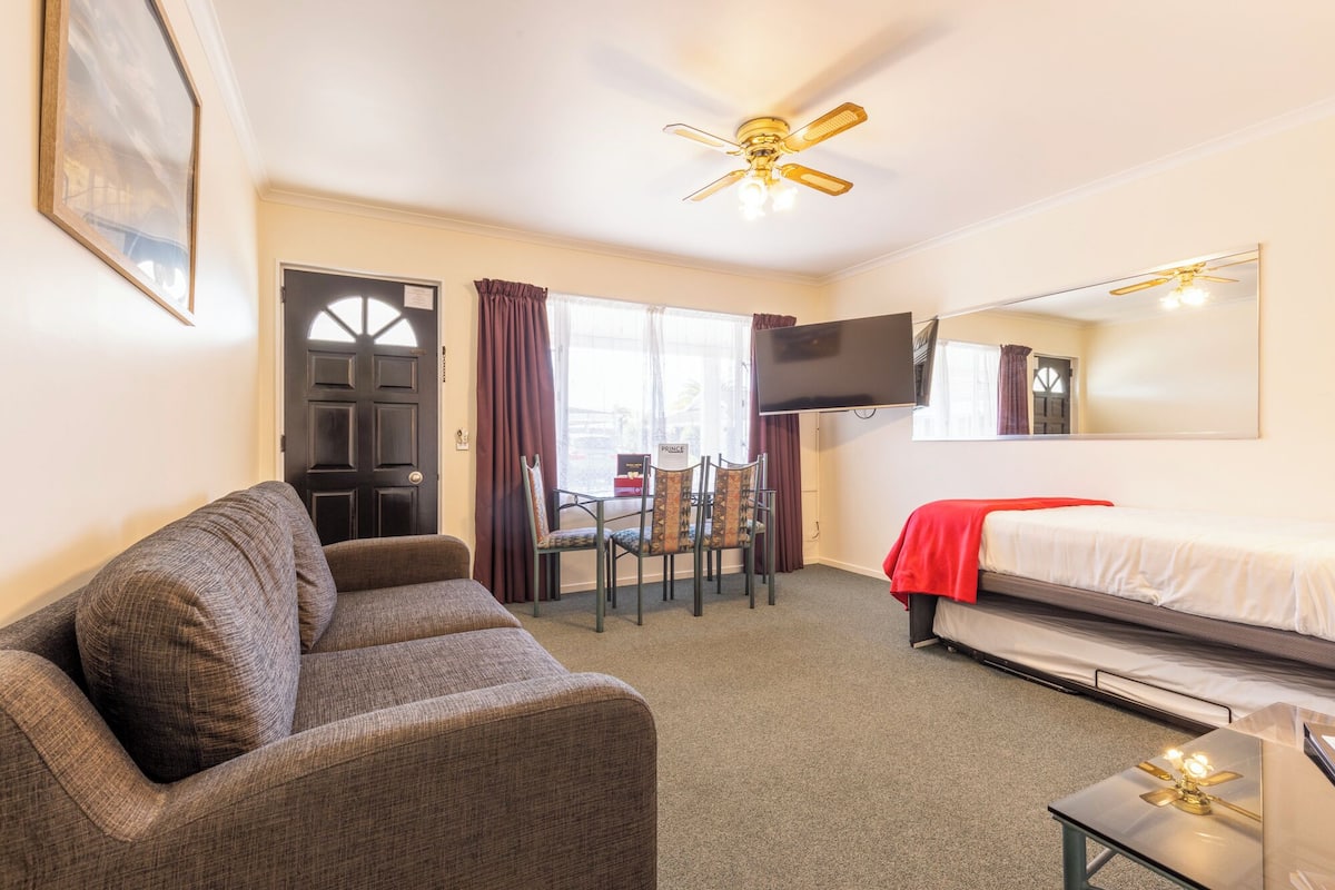 Une chambre d’hôtel équipée d’un lit, d’un canapé, d’un téléviseur fixé au mur et d’un ventilateur de plafond.