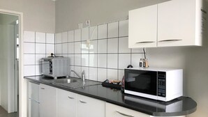 Une cuisine moderne avec des meubles blancs, un plan de travail noir, un four à micro-ondes et un grille-pain.