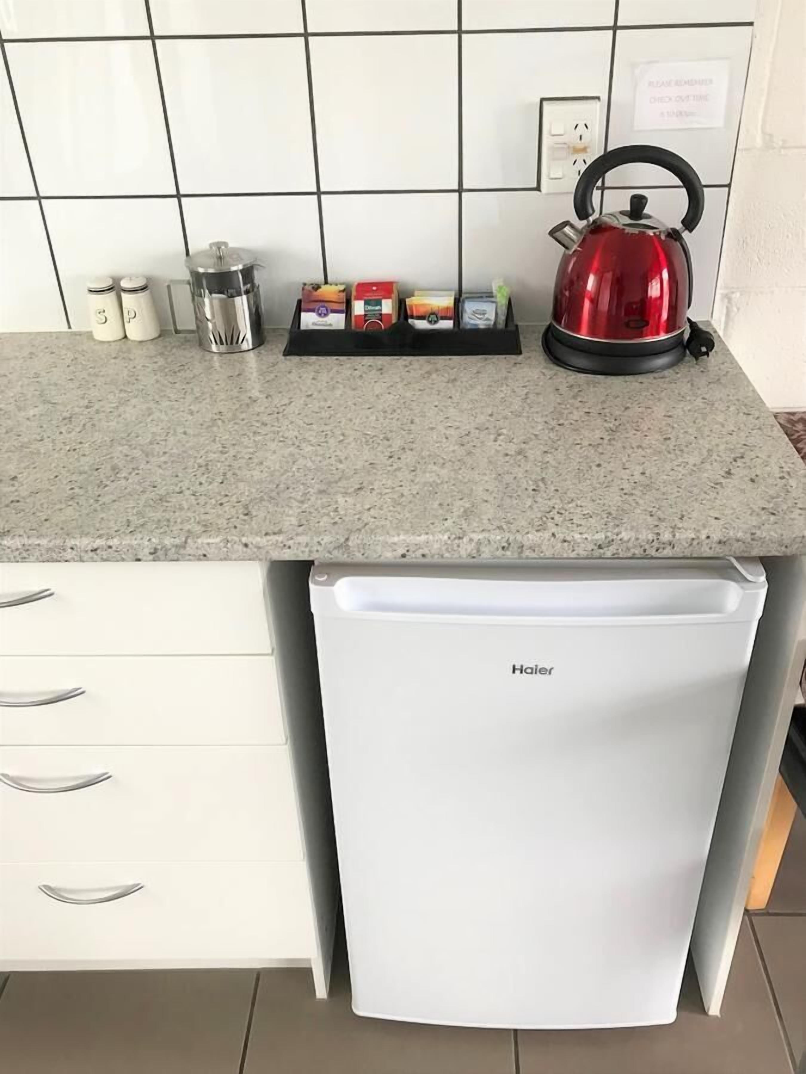 A compact kitchen with a white refrigerator, a granite countertop, and a kettle.