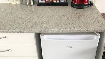 A compact kitchen with a white refrigerator, a granite countertop, and a kettle.