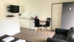 Une chambre d’hôtel moderne équipée d’un canapé, d’un téléviseur fixé au mur, d’une petite kitchenette et d’un coin repas avec une table et des chaises.