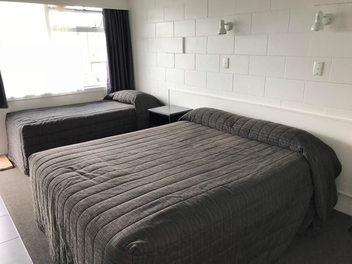 A hotel room with two beds, a small table, and a white brick wall.