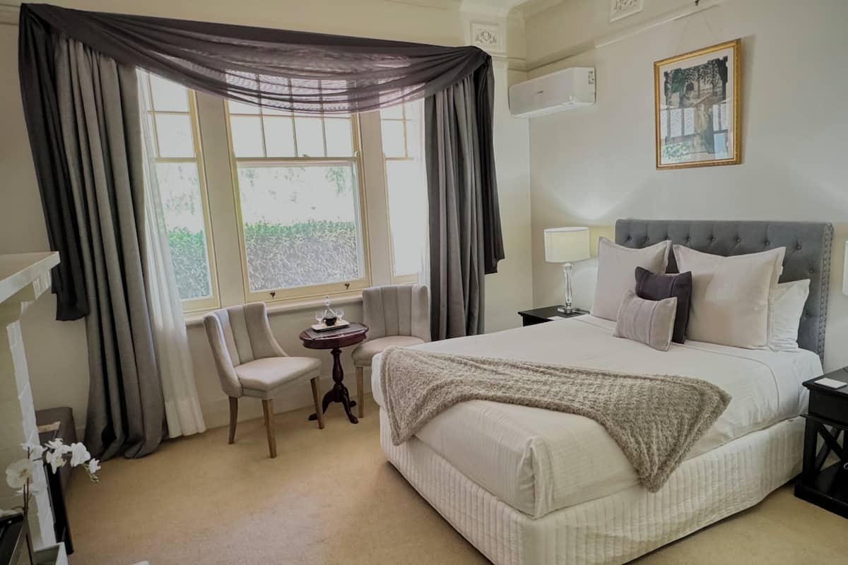 A neatly arranged hotel room with a bed, two bedside tables with lamps, a chair, and a window with curtains.