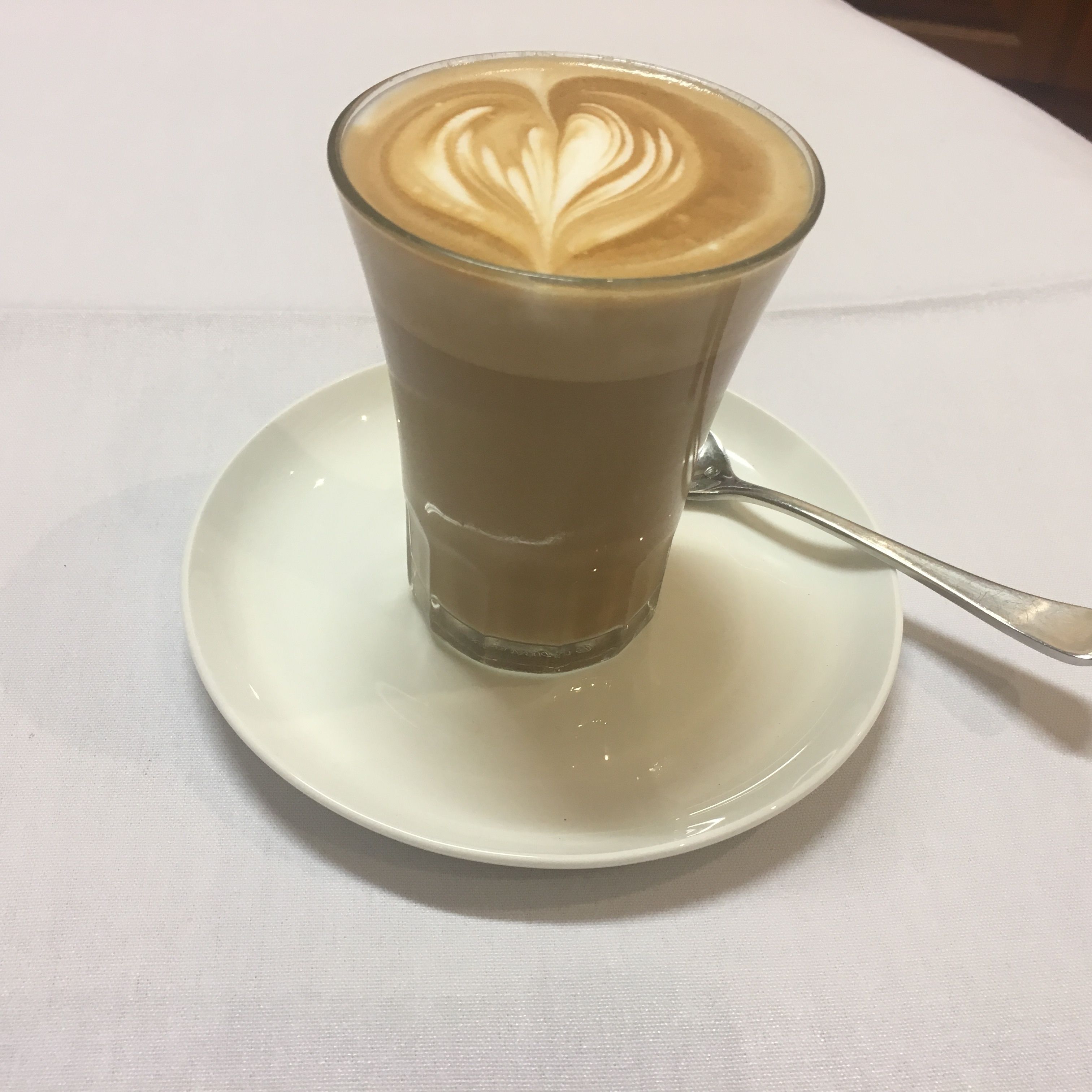 A glass of coffee with latte art on a white plate.