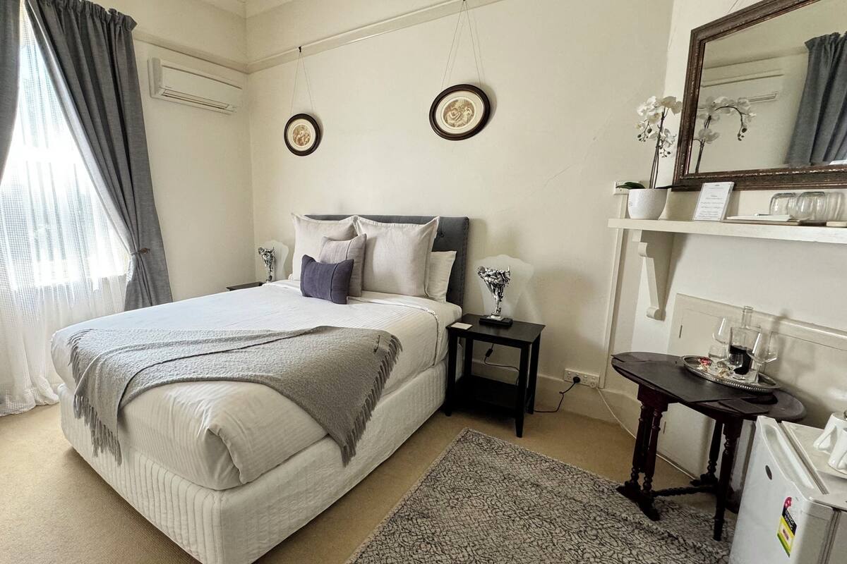 A bedroom with a bed, bedside table, mirror, and a dresser.