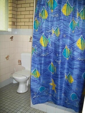 A bathroom with a blue shower curtain featuring fish and sea creatures, a white toilet, and a tiled floor.
