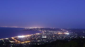 A coastal cityscape at night with a winding road along the coastline and a view of the sea.
